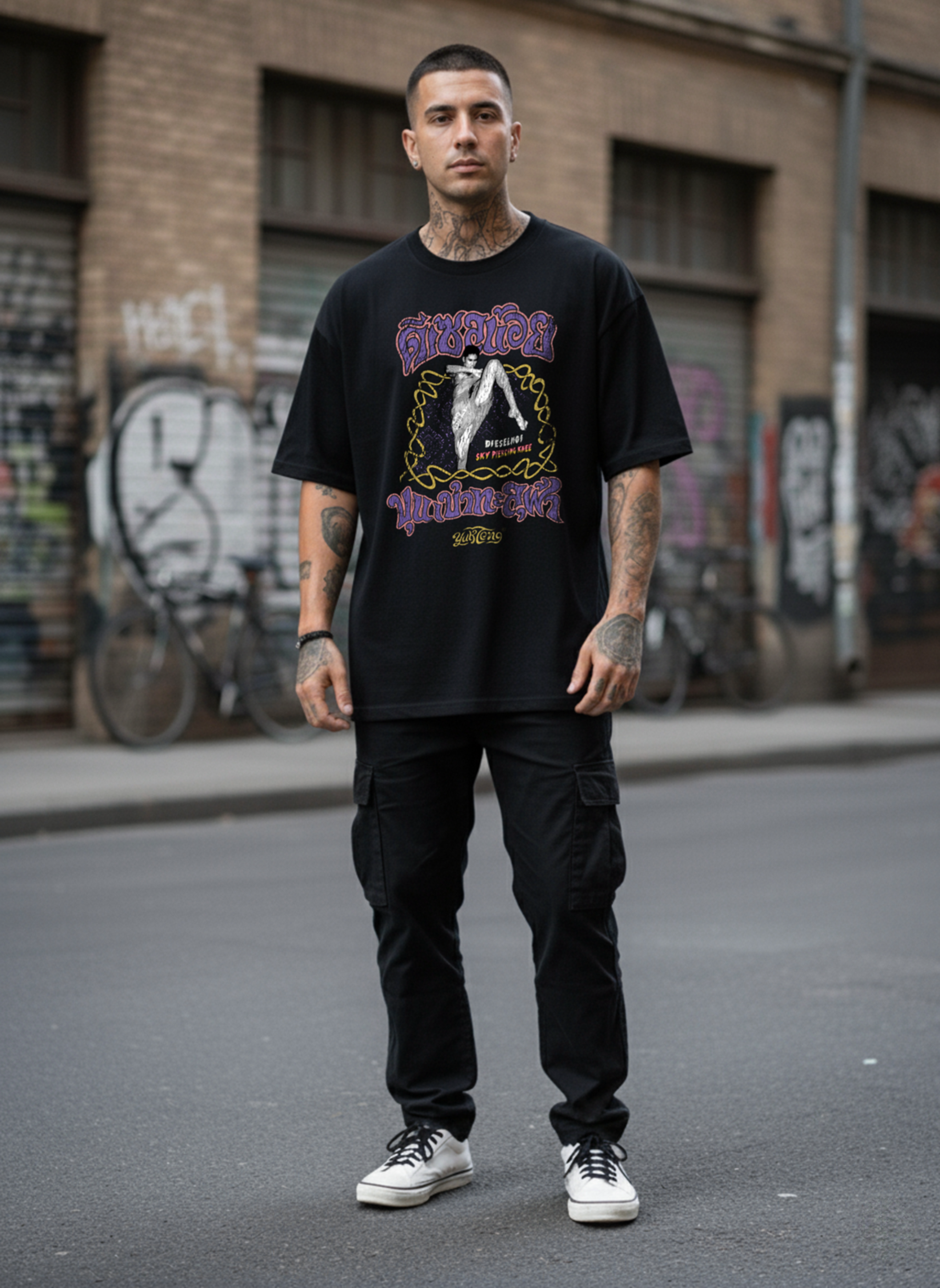 Man wearing a black graphic t-shirt and black pants standing on a street with graffiti in the background